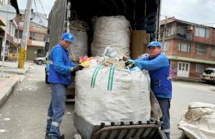 Dos personas con una bolsa de reciclaje y un camión de fondo