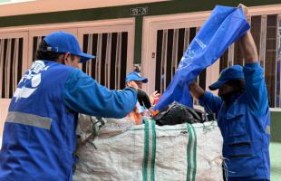 Dos personas con una bolsa de reciclaje y un camión de fondo